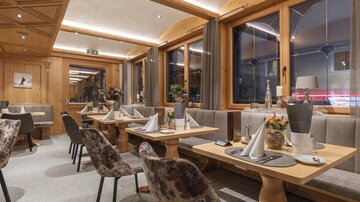 A stylish restaurant with wooden decorations and upholstered benches. The tables are elegantly set, creating a cozy atmosphere.