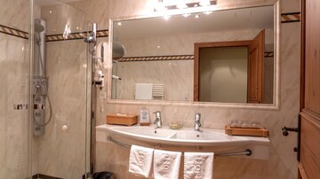 A modern bathroom with a large, elegant shower and a double washbasin. The mirror reflects the stylish decor and the bright walls.
