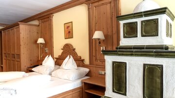A cozy bedroom with wooden paneling and two beds. A traditional tiled stove adds rustic charm to the room.