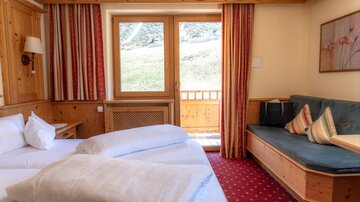 A cozy hotel room with a double bed and a seating area. Through the windows, a green landscape can be seen.