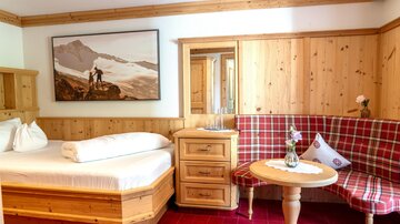 A cozy room with wooden furniture and a made bed. On the wall hangs a picture of mountains and a person enjoying the view.