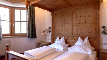 A cozy bedroom with a wooden bed and two comfortable pillows. The windows provide plenty of light, and the room is decorated in a rustic style.