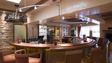 An elegant bar with a wooden counter and stylish chairs. In the background, bottles and glasses are neatly arranged.