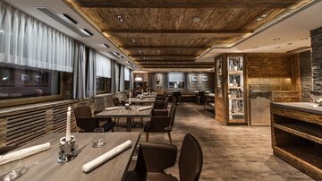 An elegant restaurant with wooden furniture and warm light. The tables are set for guests, creating a cozy atmosphere.