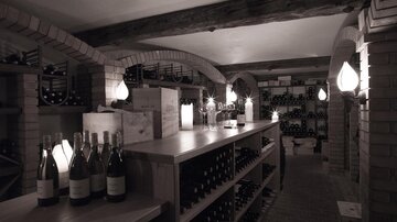 A stylish wine cellar with wooden tables and shelves full of wine bottles. Soft lighting creates a cozy atmosphere.