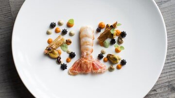 An elegant dish on a white plate, primarily made of seafood. It is artistically decorated with various side dishes.